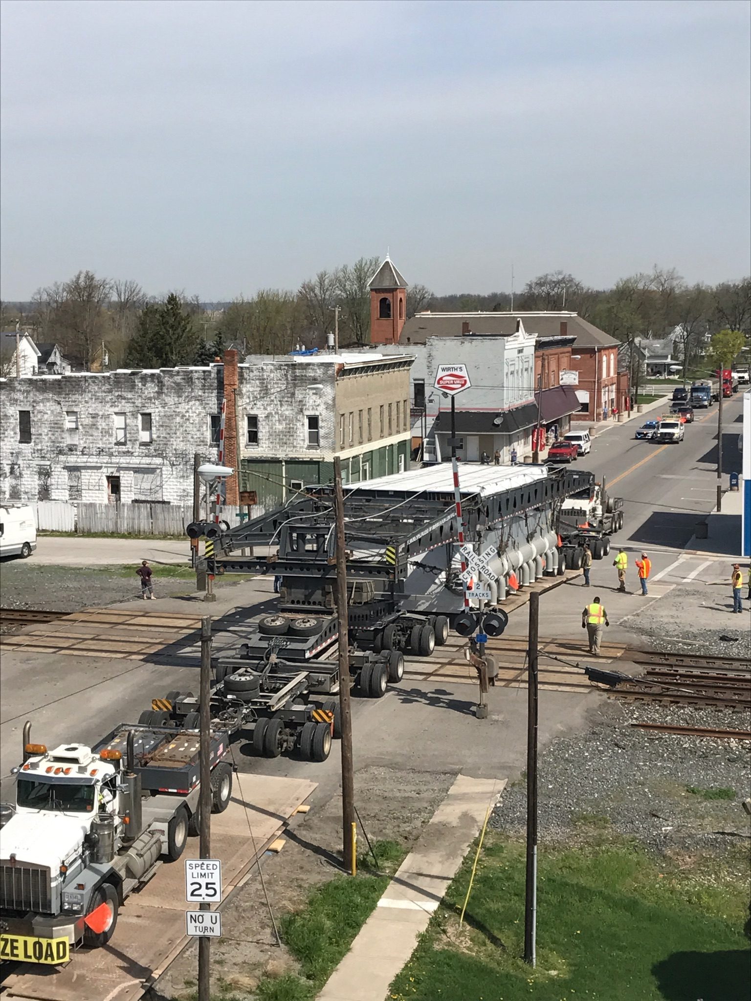 Superload on multi-axle trailer crossing railroad tracks through a small downtown with police escort