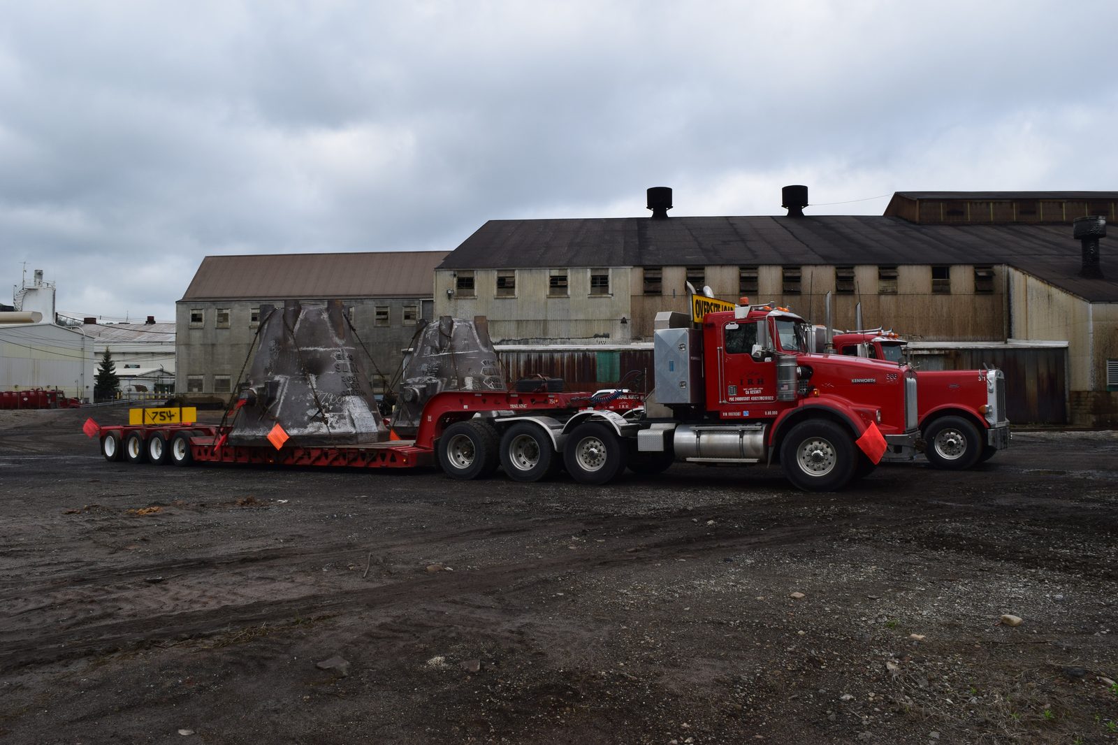 Steel foundry slag pots chained to a lowboy trailer pulled by a heavy Kenworth tractor